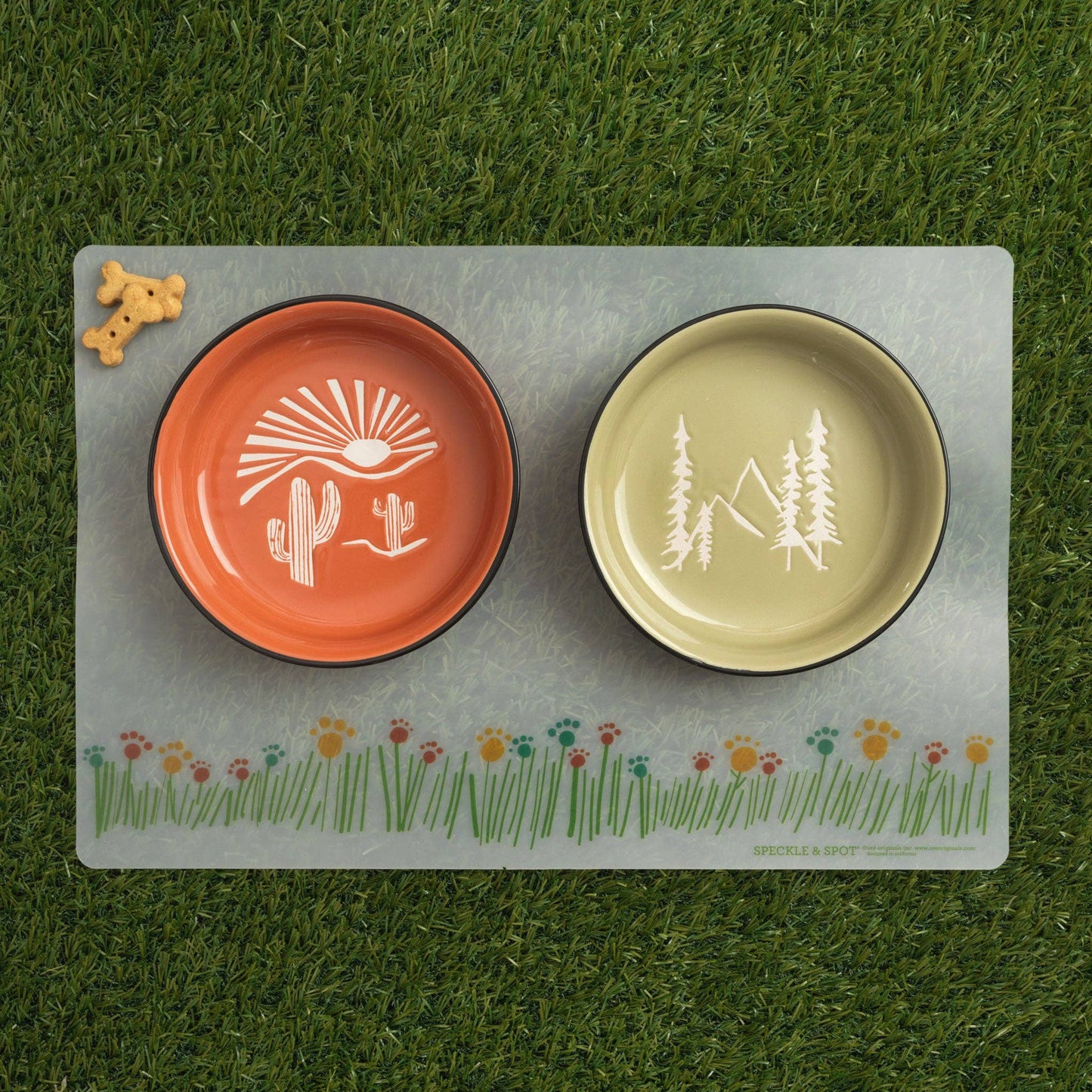 Two pet bowls with nature-themed designs on a placemat with a grass pattern.