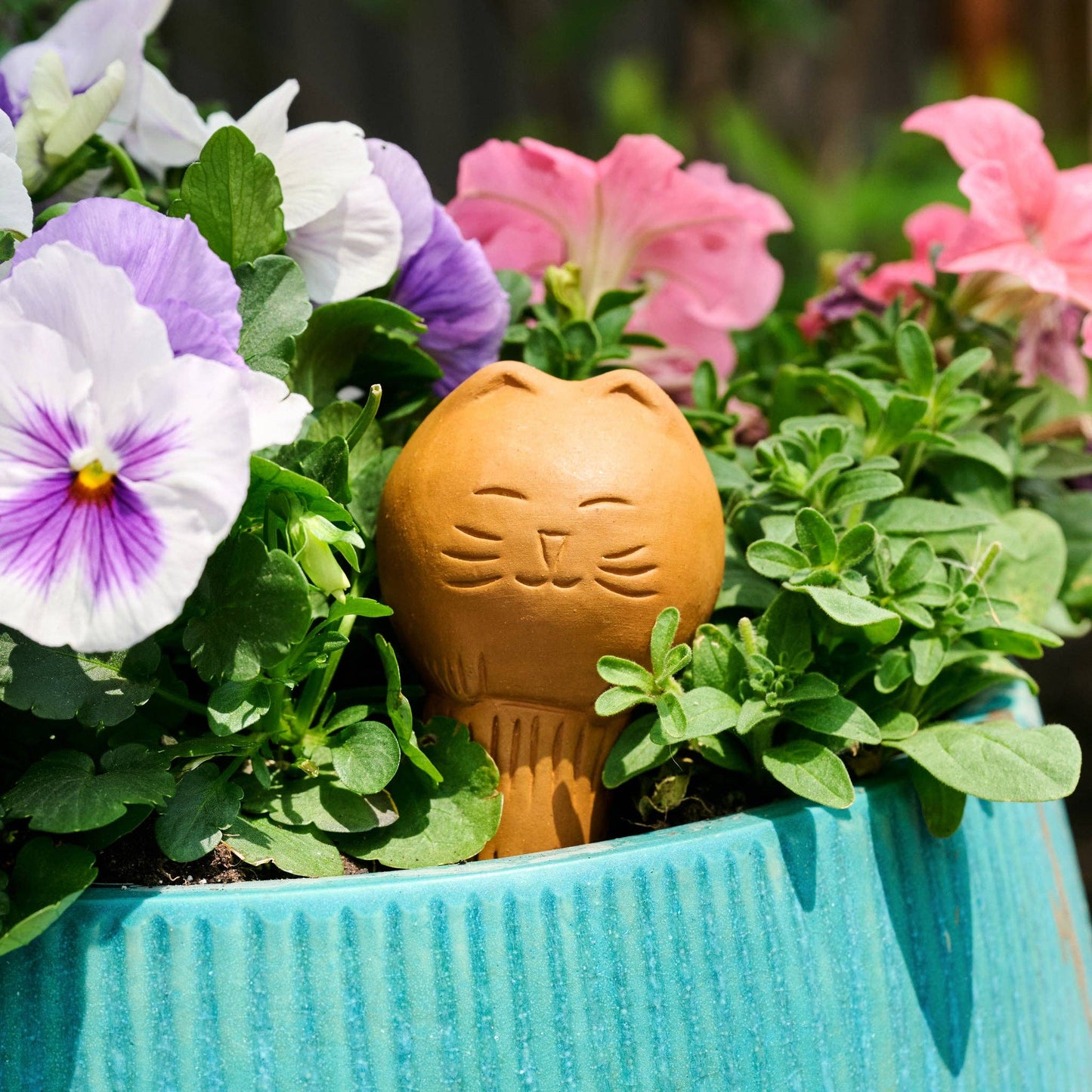Cat-shaped watering device among potted flowers with a blurred background
