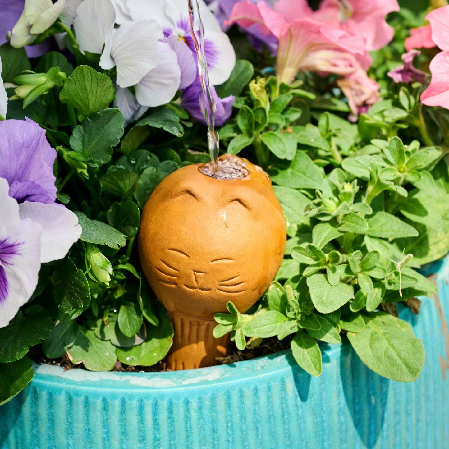 Terracotta cat-shaped watering device in potted plant being filled with water