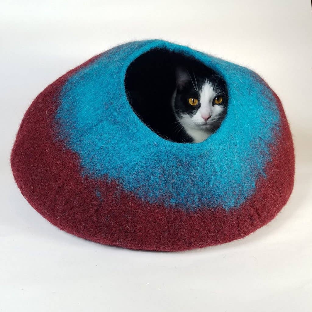 A cat sitting inside a maroon and teal colored cat cave.