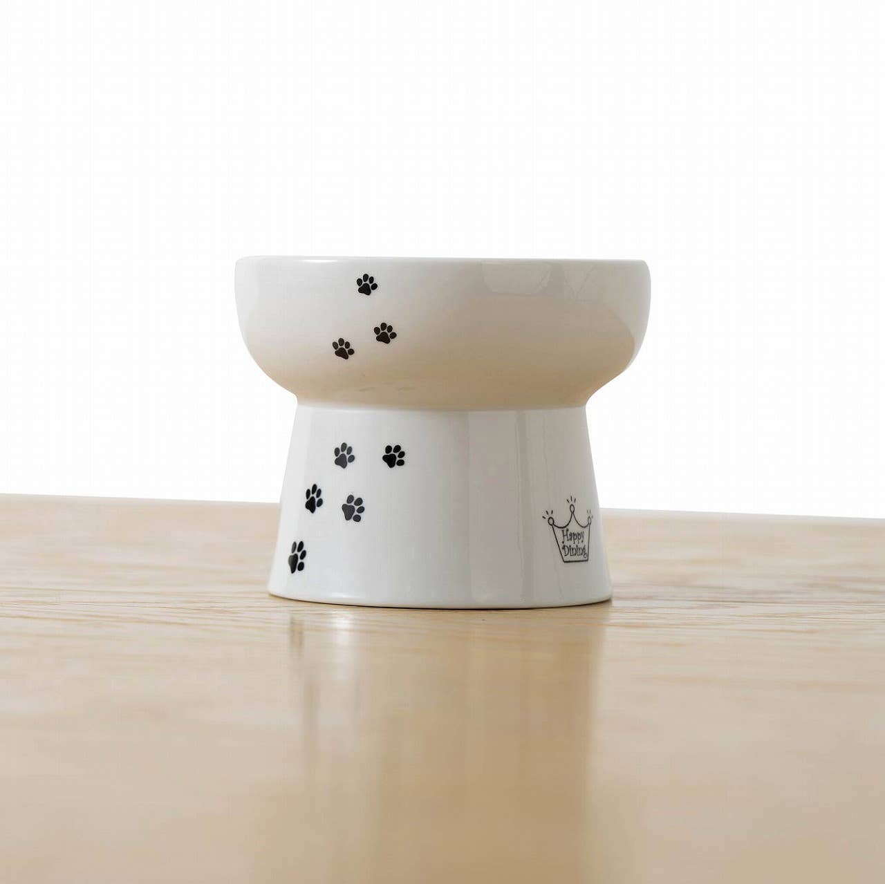 White ceramic pet bowl with black paw prints on a wooden surface
